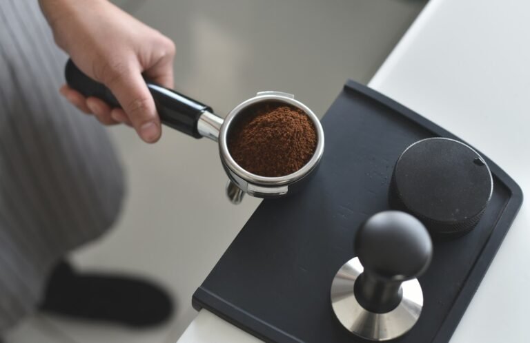 Portafilter with ground coffee next to a tamper